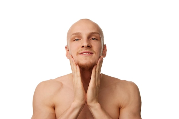 肌肉のある肌のないハンサムな頭皮の若い男が白いスタジオに隔離された顔を洗っている
