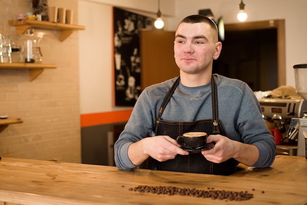 Handsome barista holding a cup of coffee at the cafe