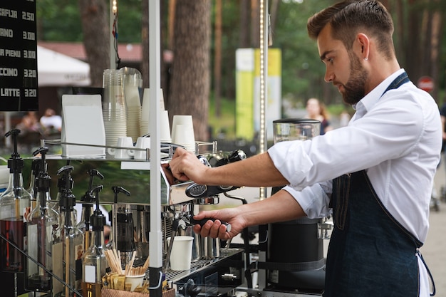 彼の移動可能な通りのコーヒーショップでの仕事中のハンサムなバリスタ男