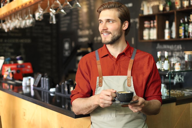 Handsome barista offering a cup of coffee to camera at the coffee shop