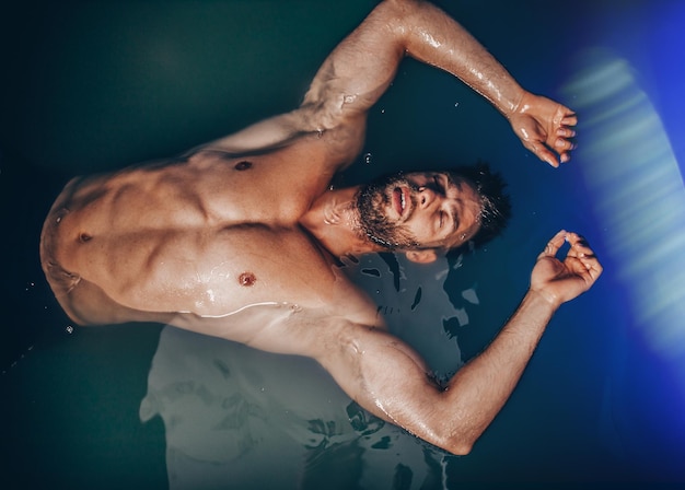 Handsome beard man floating in tank filled with dense salt water used in meditation, therapy, and alternative medicine.