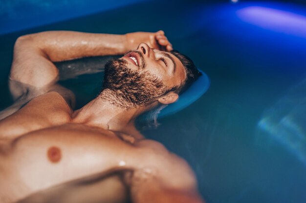 瞑想、治療、代替医療で使用される濃い塩水で満たされたタンクに浮かんでいるハンサムなひげの男。