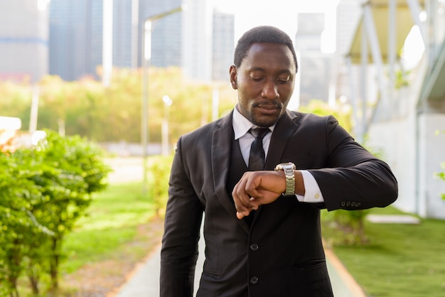 Handsome bearded African businessman in suit checking the time at the park