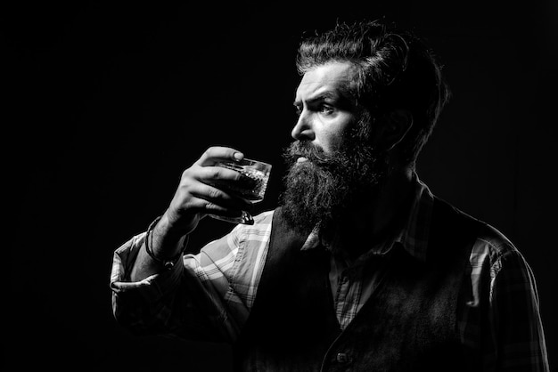 Handsome bearded businessman is drinking expensive whisky Confident bearded man in black suit with glass of whisky in loft