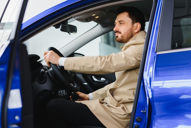 Handsome bearded businessman is sitting in a new car in car dealership