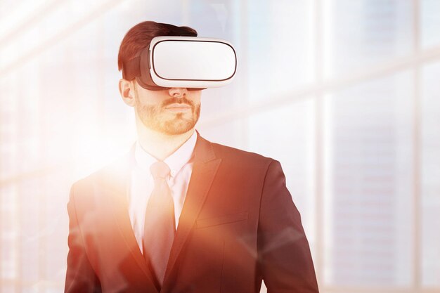 Handsome bearded businessman wearing vr glasses and suit standing over skyscraper background. Hi tech concept. Toned image