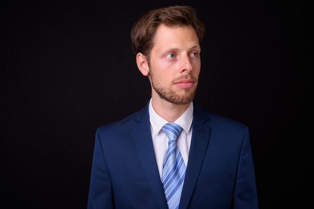 handsome bearded businessman with brown hair wearing suit against black space