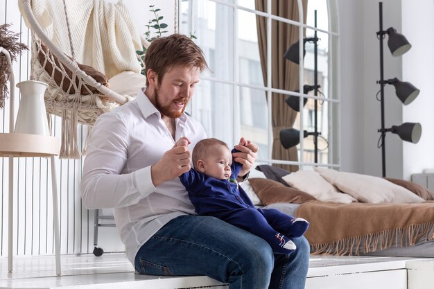 Handsome bearded father playing with his little baby boy in a beautiful interior