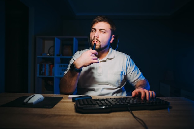 Handsome bearded freelancer man works at night at home in the\
bedroom on the computer and smokes