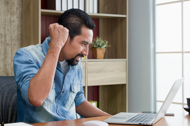 Handsome bearded guy raised fisting expressing confidence while using the laptop.