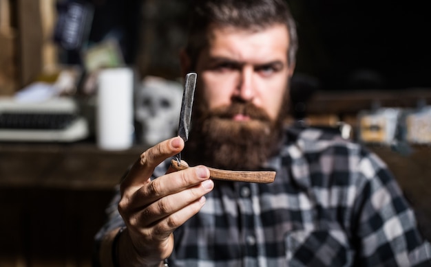 Handsome bearded hairdresser is holding a straight razor while at the barbershop