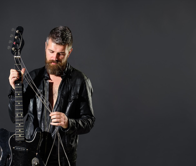 Handsome bearded in leather jacket with electric guitar man\
with beard holds musical instrument