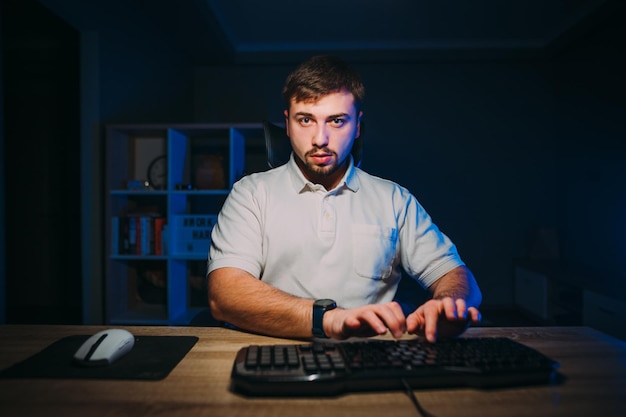 Handsome bearded male programmer working at night at home on
computer in room with blue light