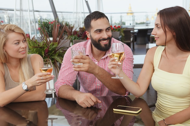 Handsome bearded man chatting with his female friends, drinking at bar terrace