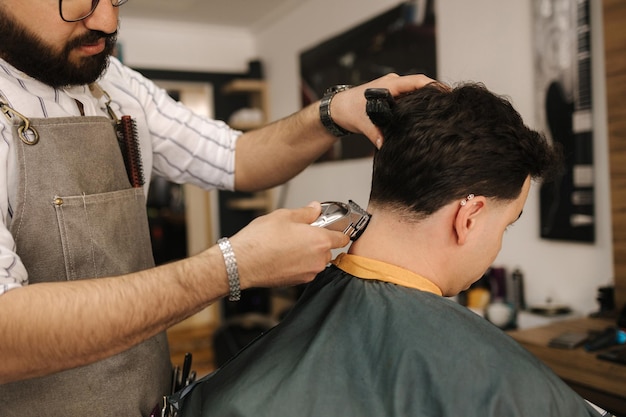 Handsome bearded man cutting hair of confident male client in berber shop