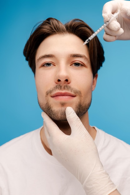 Handsome bearded man getting beauty injections Isolated on blue background Beauty care anti aging procedures plastic surgery concept