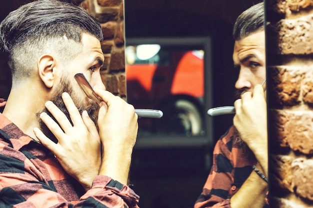 Handsome bearded man hipster with stylish haircut and beard holding old fashion razor in red checker...