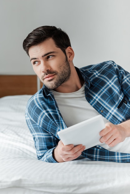 Handsome bearded man holding digital tablet on bed