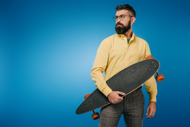 Handsome bearded man holding longboard isolated on blue