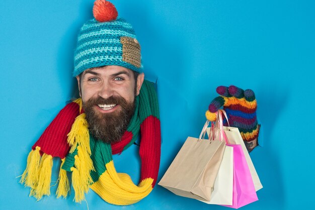 Handsome bearded man holds shops packet in hand through a paper hole bearded man in warm colourful