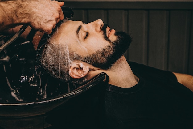 A handsome bearded man is having his hair washed by hairdresser at the barbershop customer service