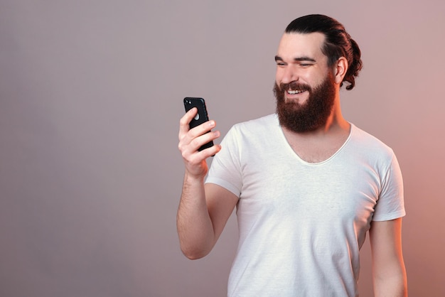 L'uomo barbuto bello sta guardando un telefono mentre sorride ampiamente