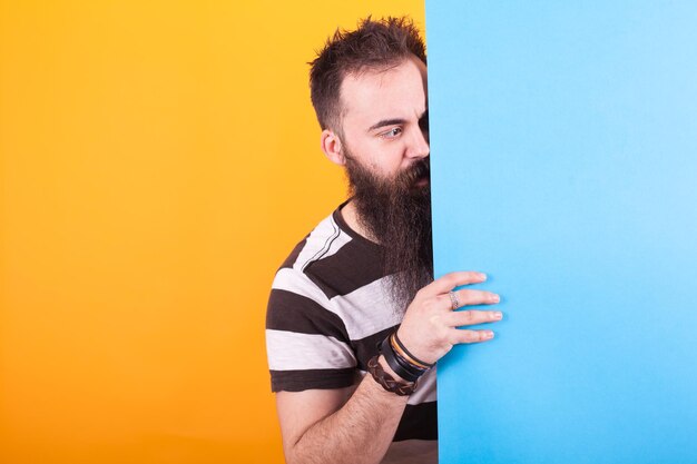 Handsome bearded man looking at a blue copy space over yellow background person