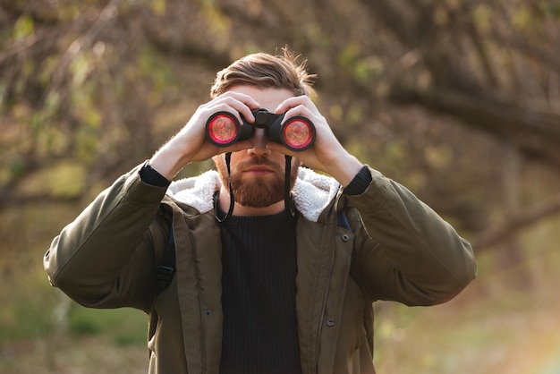 Photo handsome bearded man looking at field-glass standing in the forest