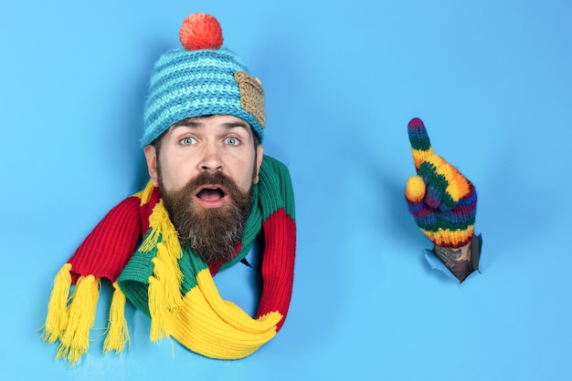 Handsome bearded man points through paper hole bearded man in warm colourful clothes looking through