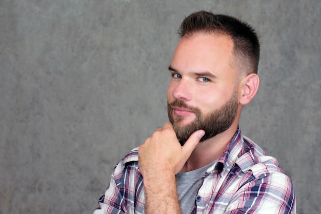 Handsome bearded man in a shirt, looks with intrigue and interest into the camera on gray