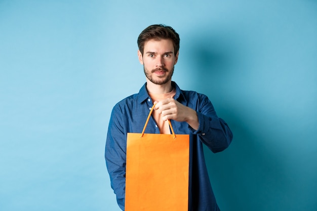 Handsome bearded man stretch out hand with orange shopping bag