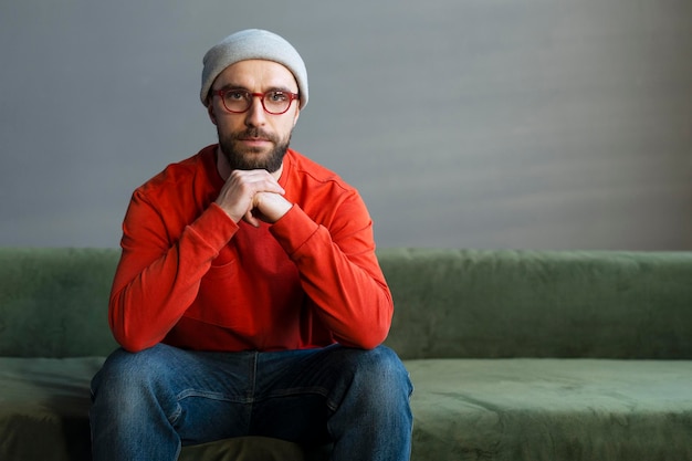 Handsome bearded man wearing trendy glasses sitting on sofa at workplace looking at camera