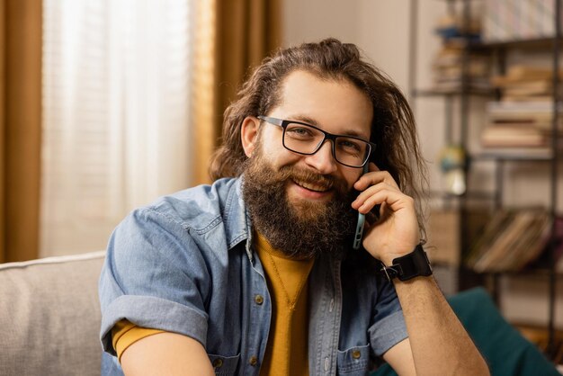 A handsome bearded man with glasses is talking on the phone the model looks into the camera