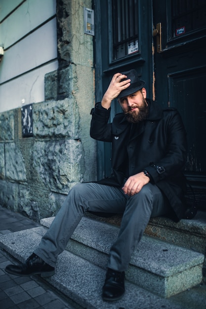 Foto uomo barbuto bello con i baffi che ritornano a casa da lavoro, sedentesi sulle scale.