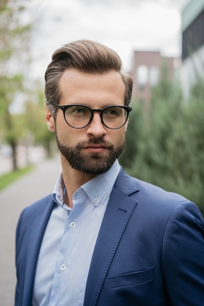 Handsome bearded man with stylish hair wearing business suit glasses looking away on the street