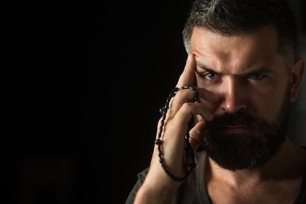 Handsome bearded man with stylish hairstyle with rosary beads in hand symbol prayers religion belief