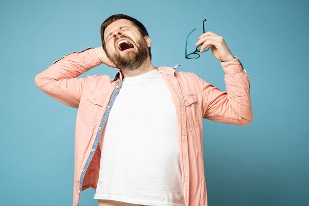 Handsome bearded man yawns funny and stretches holding glasses in his hands