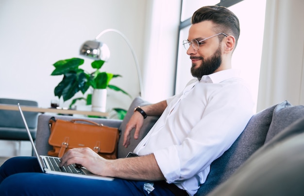 handsome bearded stylish business man while he is working in the laptop and sitting on the couch