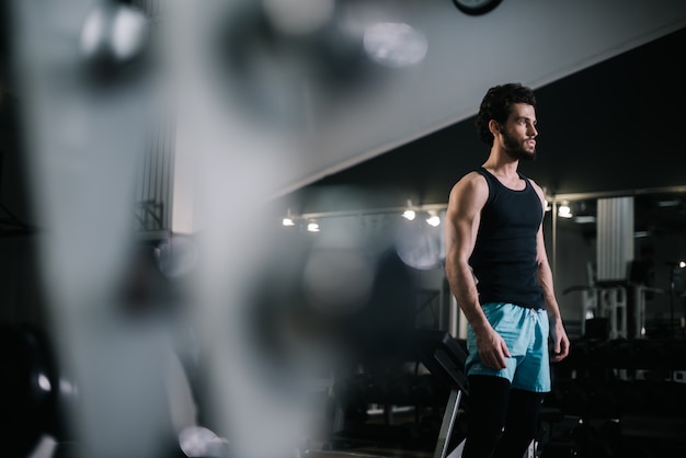 Handsome bearded young man with muscular wiry body wearing sportswear standing in modern dark gym