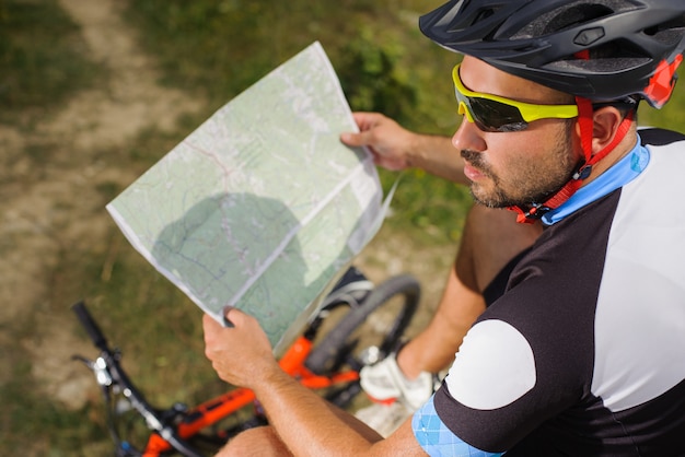 Handsome bicyclist with route map on the top of rock