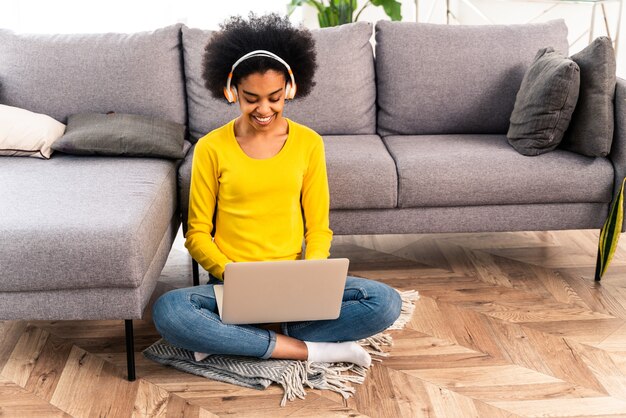 Handsome black adult woman at home listening music online with computer laptop and headphones - Pretty black girl working in remote online at home