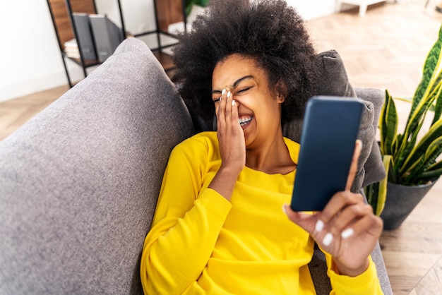 Handsome black adult woman at home watching video online on social network app with smartphone - Pretty black girl working in remote online on mobile phone