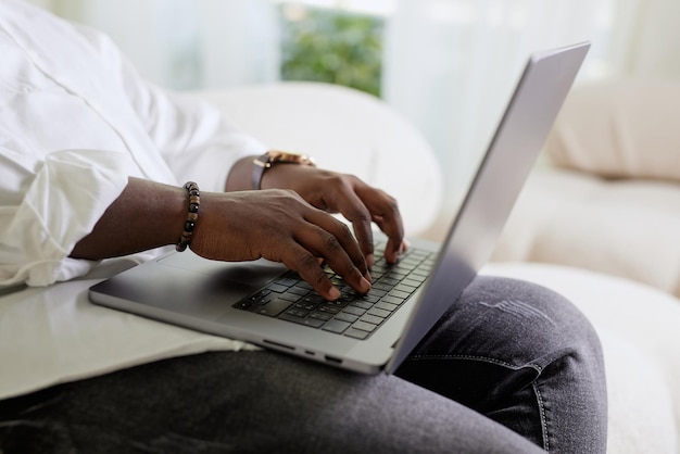 Handsome Black African American Man Working on Laptop Computer while Sitting on a Sofa in Cozy Livin