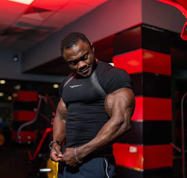 Handsome black fitness model man shows strong hands to the\
camera modern gym background