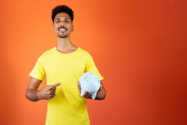 Uomo nero bello che tiene un salvadanaio isolato su orange uomo in una camicia gialla isolata