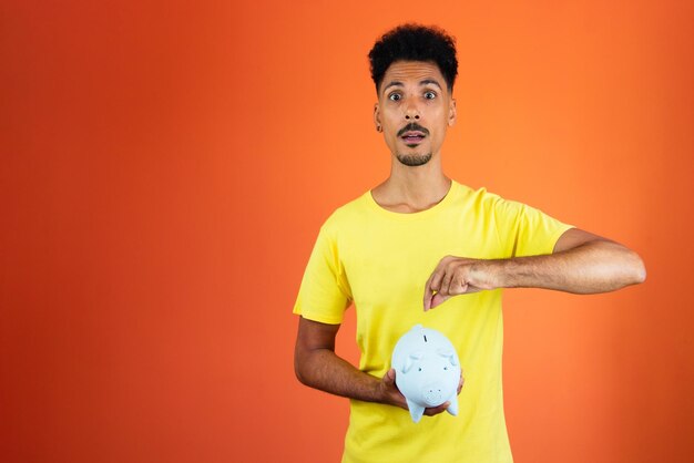 Handsome Black Man Holding a Piggy Bank Isolated on Orange Man in a yellow shirt isolated