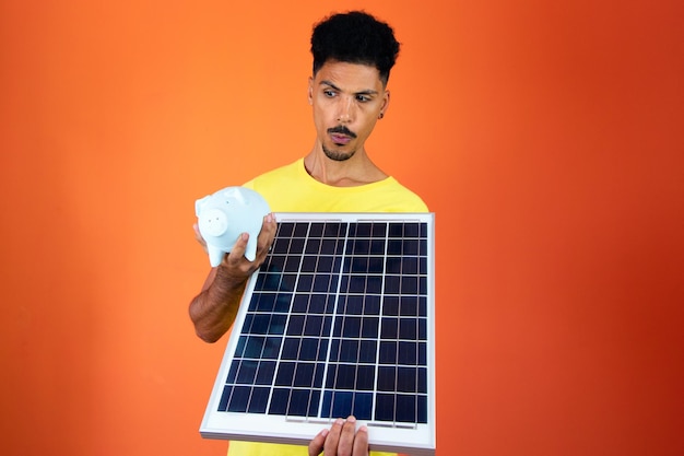 Handsome Black Man Holding a Piggy Bank and Solar Panel Isolated on Orange Man in a yellow shirt isolated