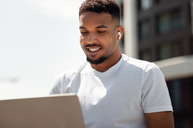 Handsome black man with wireless earphones working on laptop freelancer sitting in urban city area