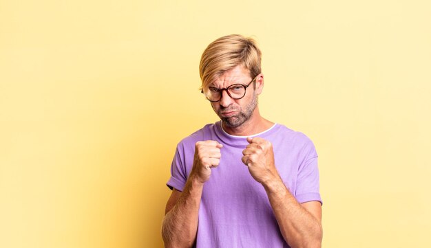 handsome blond adult man looking confident, angry, strong and aggressive, with fists ready to fight in boxing position