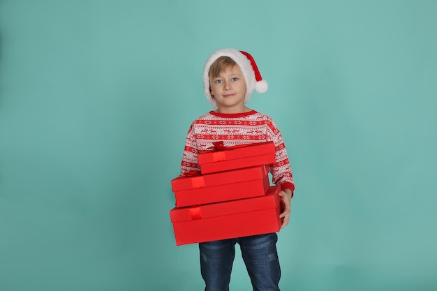 a handsome blond boy in a Christmas sweater Santa Claus hat holds gift boxes in his hands